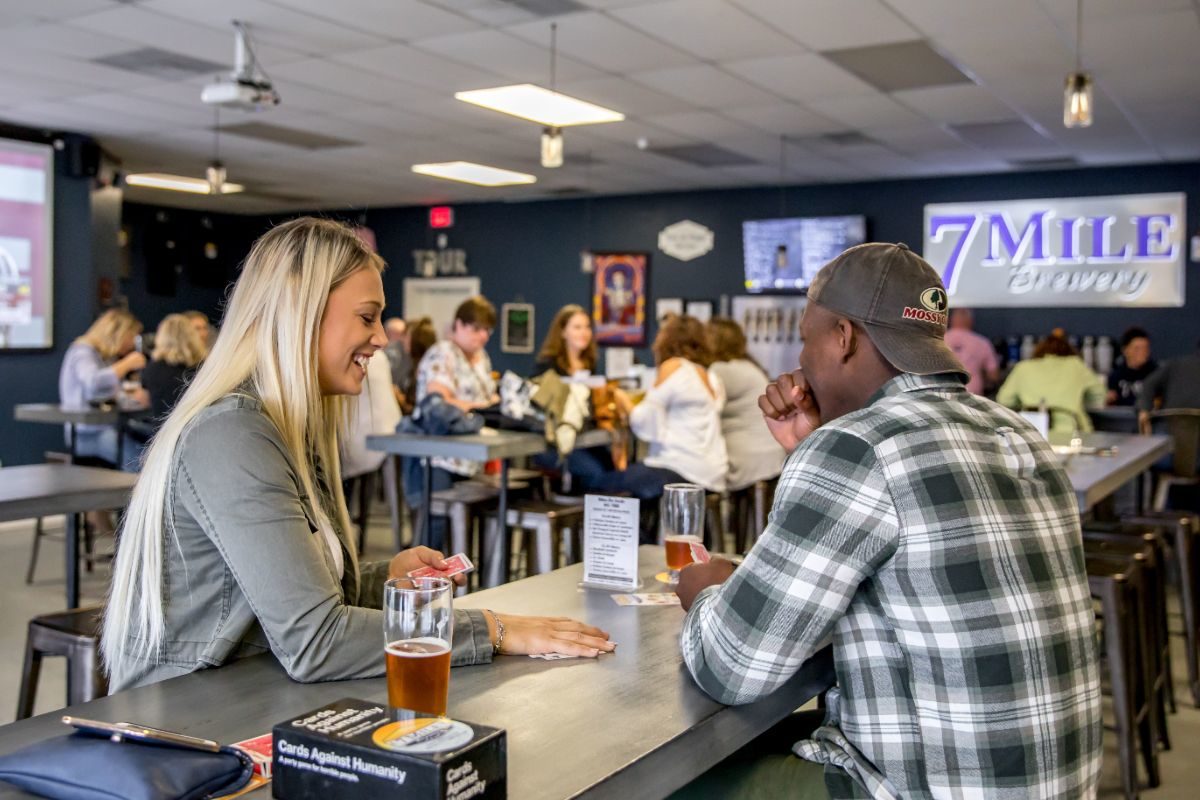A couple playing cards and laughing while enjoying 7 Mile beer at the Brewery