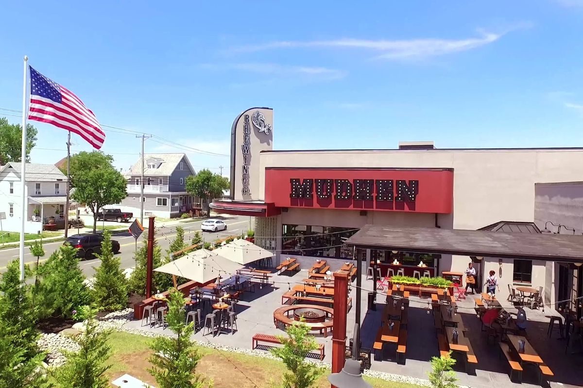 Drone shot of the outdoor picnic tables and fire pits with awnings, shades and string lights at Mudhen Brewery in Wildwood NJ