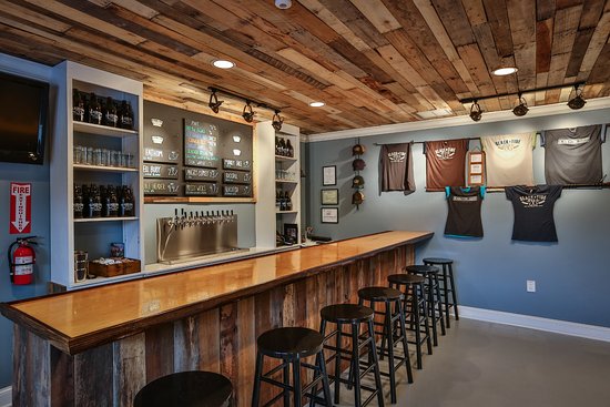 The tasting room at Slack Tide Brewing Co with stools and live edge wood bar top with beer list, taps and t-shirts on the wall