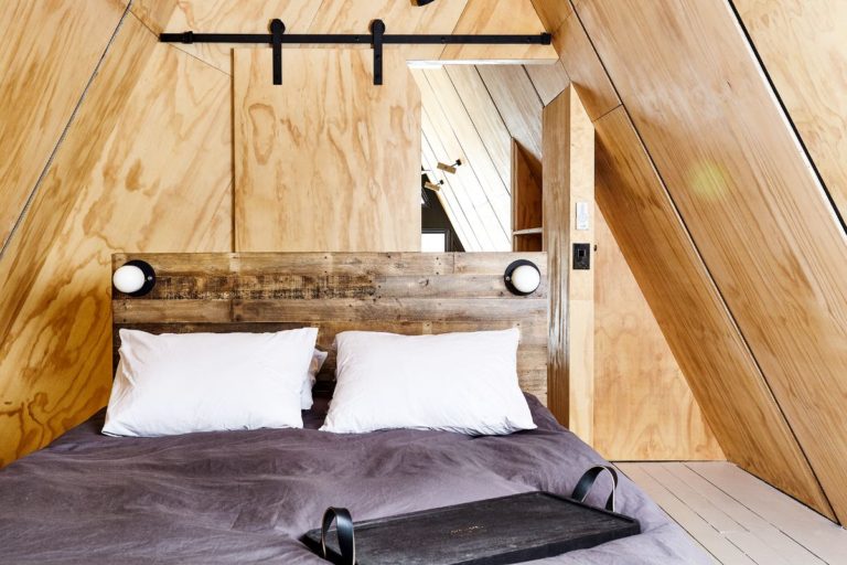 Queen bed with lights built into headboard in Aframe with walls clad in plywood