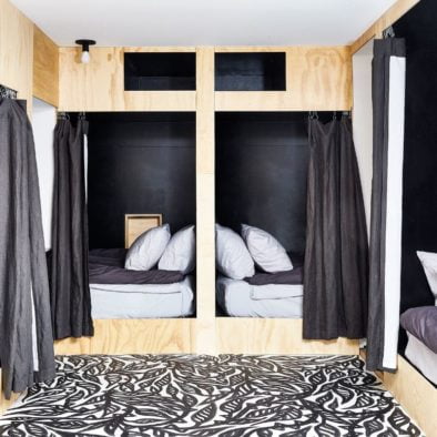 Bunk room with 4 single beds in plywood clad nooks with curtains and artist painted black and white flowers on floor