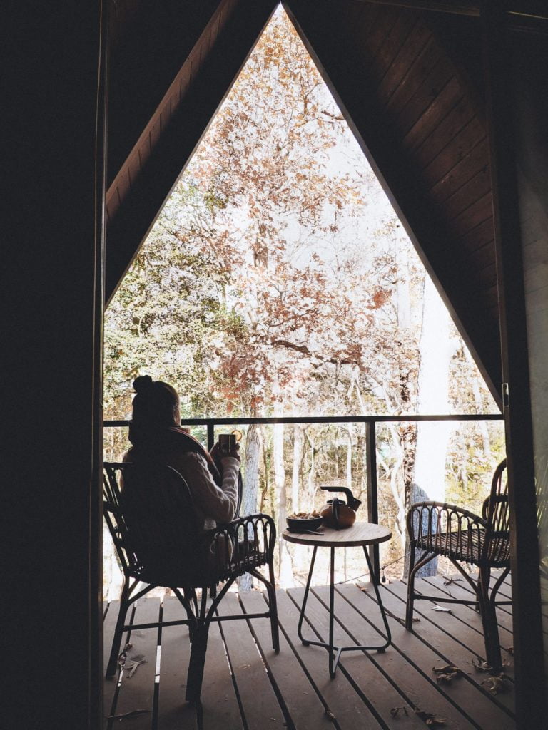 Woman sipping tea on top deck of Aframe Cabin overlooking woods