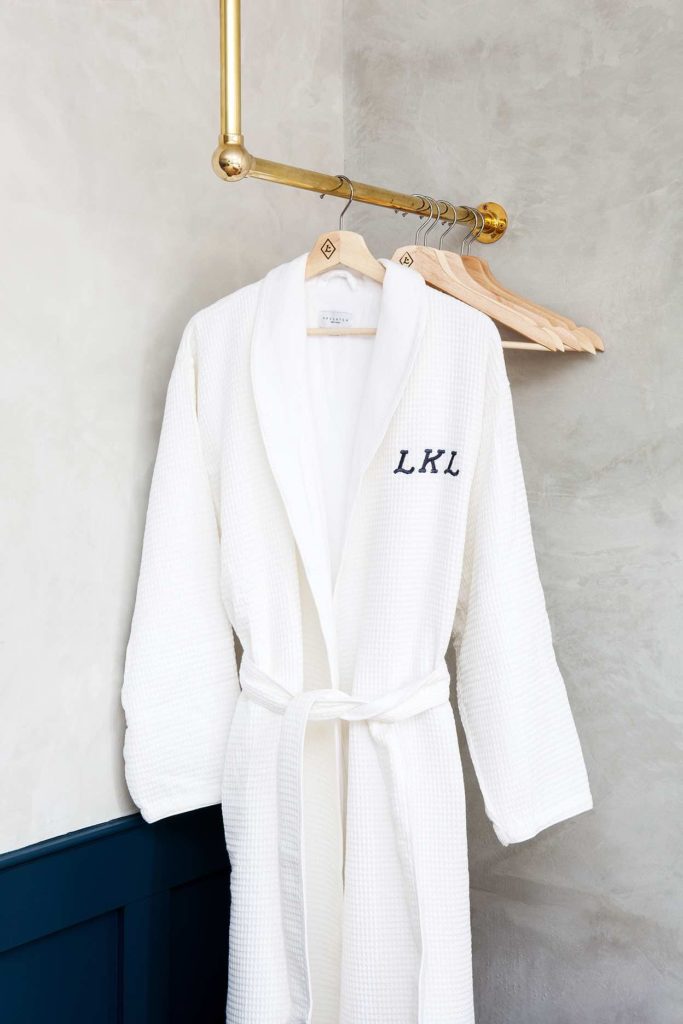 Plush white robes with Lokal Hotel Logo hanging in hotel room on brass bar