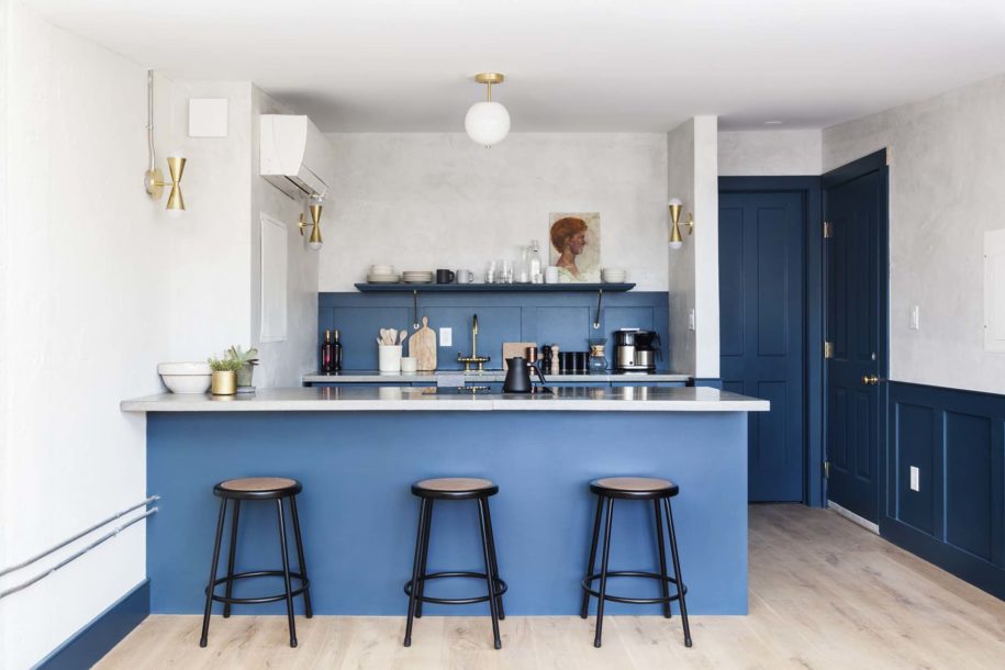 The Kitchen with island and three stools at the Ben Suite in Lokal Hotel Old City is blue with brass fixtures and a single open shelf with oil portrait