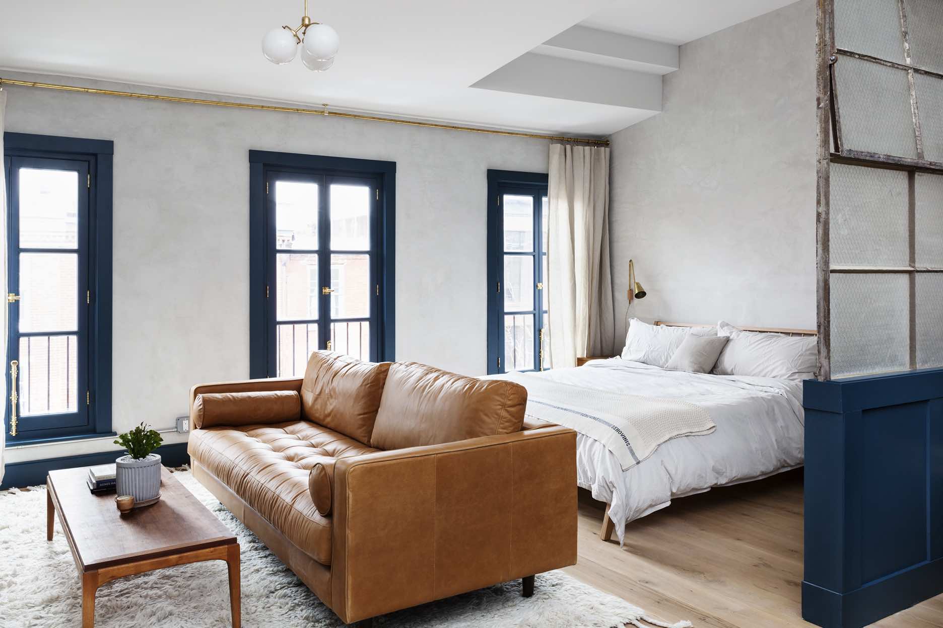 Large top floor suite at Lokal Hotel Old City with three floor to ceiling operable historic windows a king bed a leather couch and vintage coffee table on top of a plush area rug