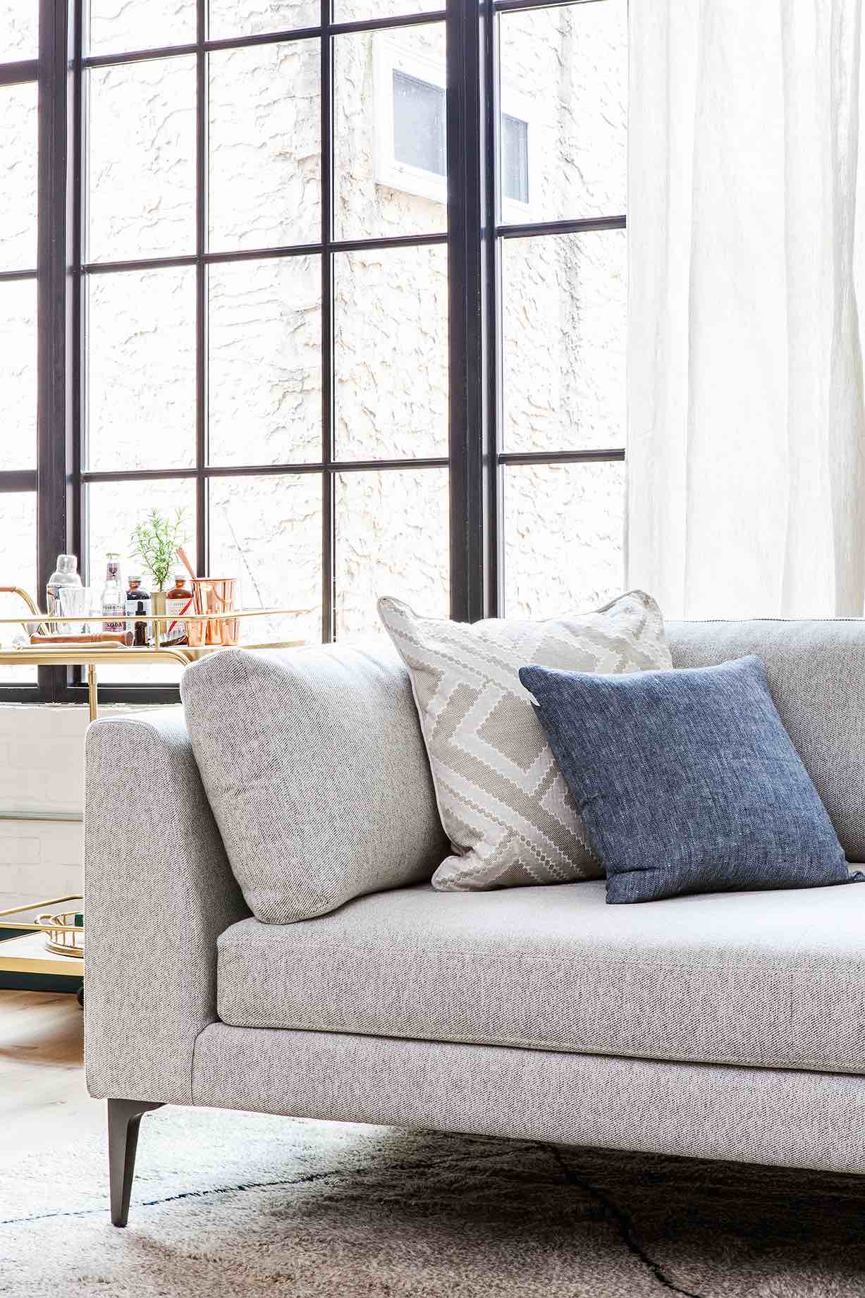 A light gray sofa with pillows in front of a large window.