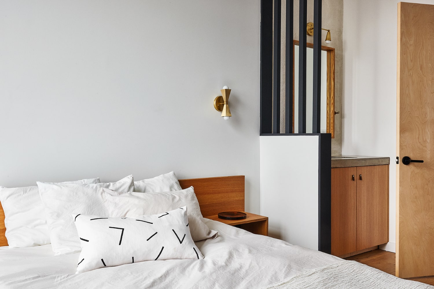 A neatly made bed with white bedding and pillows, a wooden headboard, and a nightstand with a cabinet beside it.