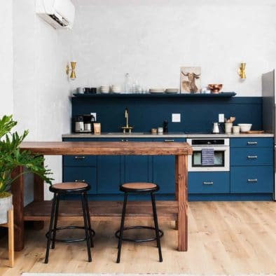 Blue kitchen in apartment hotel room by Lokal Hotel with brass hardware, wide plank white oak floors and custom wooden island with school stools