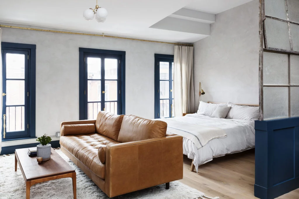 A wide view of a hotel suite with a leather sofa, wood coffee table, and a bed with white linens.