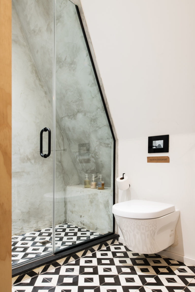 The upper bathroom at the Lokal Aframe with black and white concrete tile, concrete walls, glass shower with matte black hardware and wall mounted toilet