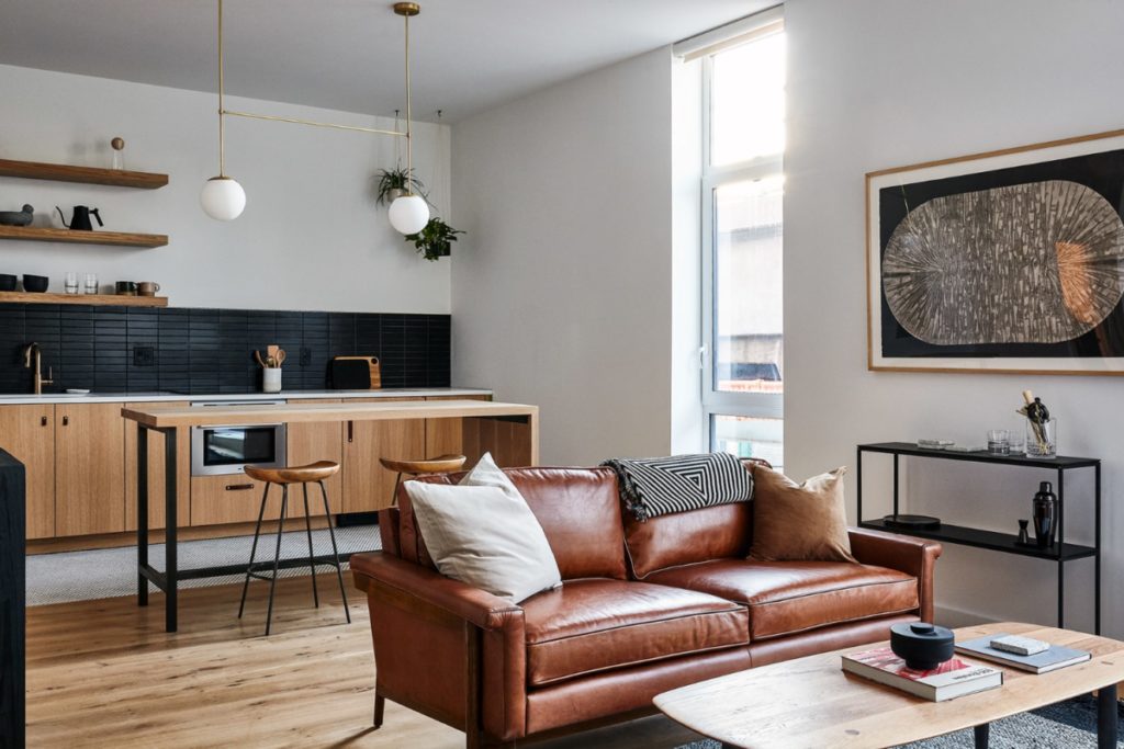 lokal hotel fishtown room with plush leather couch, art above a small bar, light pouring in a full height window and kitchen with island in the background