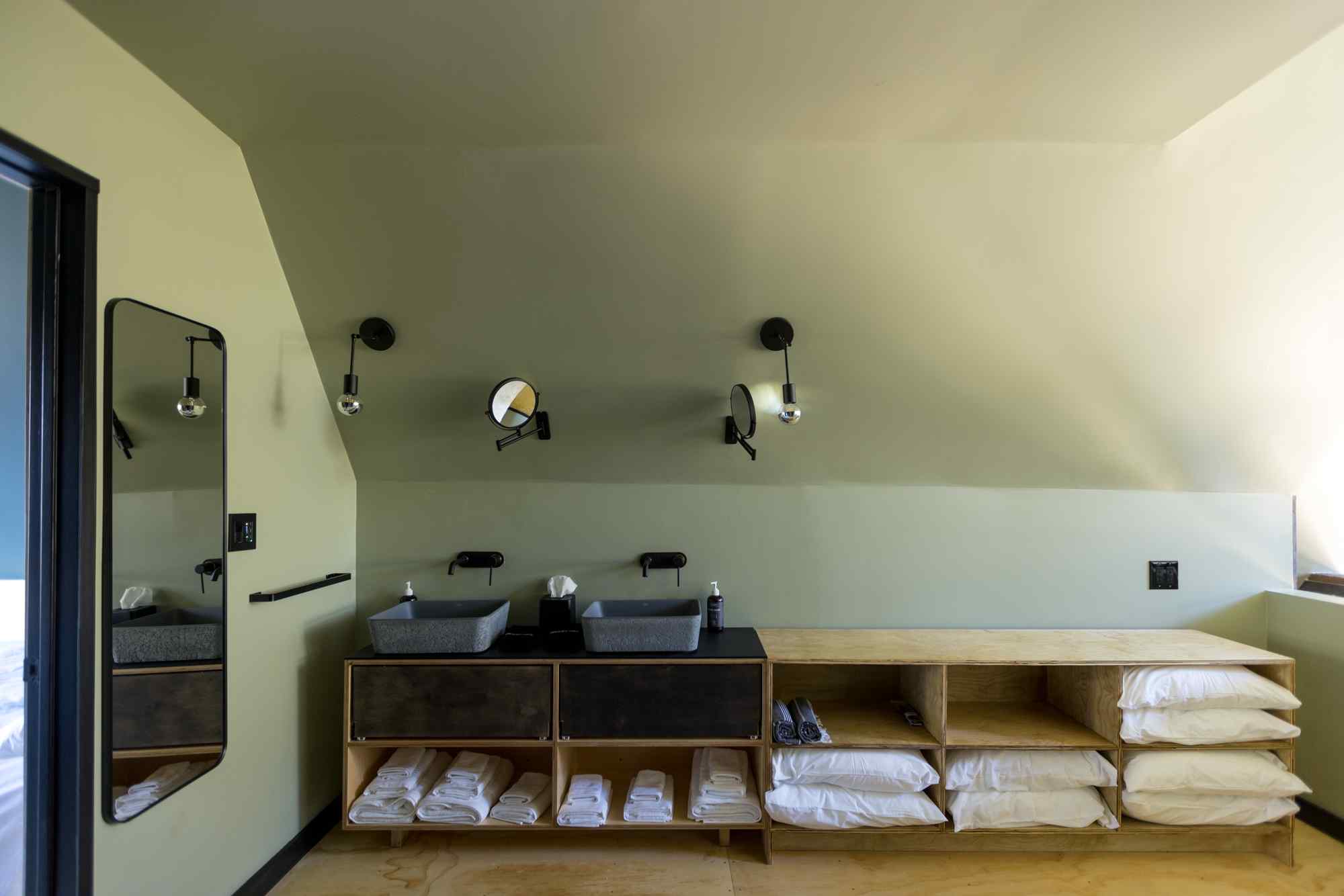 A bathroom with a double vanity, towels, pillows, and a mirror