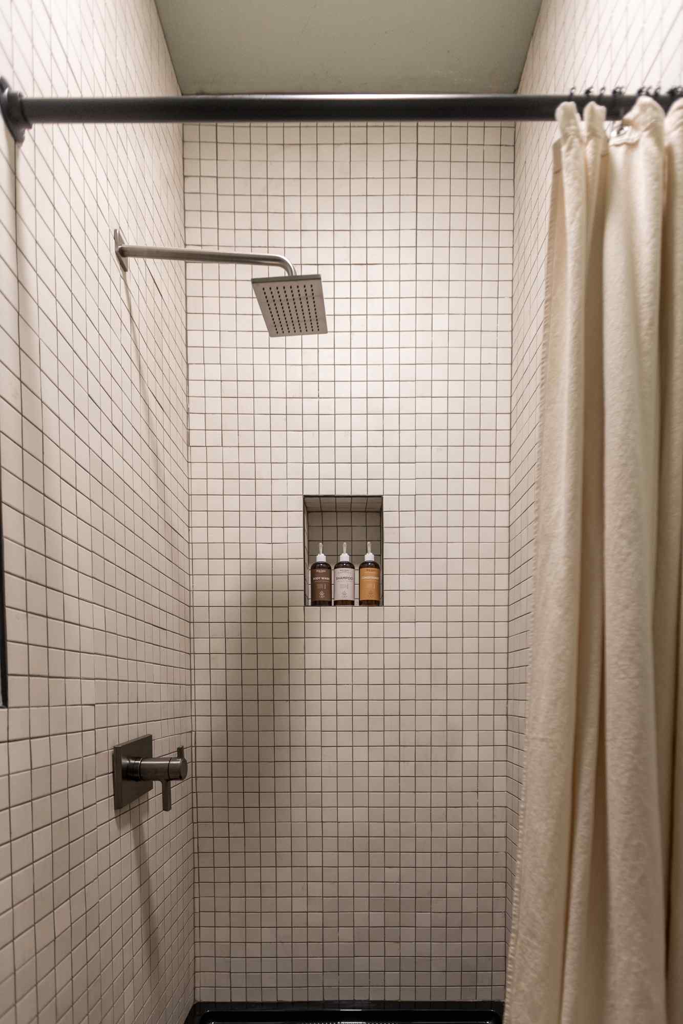 A shower with white tiles, a shower curtain, and a shower head