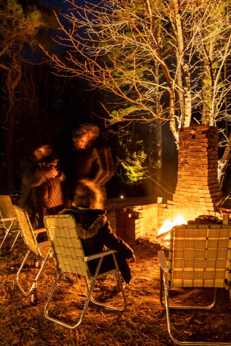Friends in the woods sitting around a camp fire in vintage folding chairs