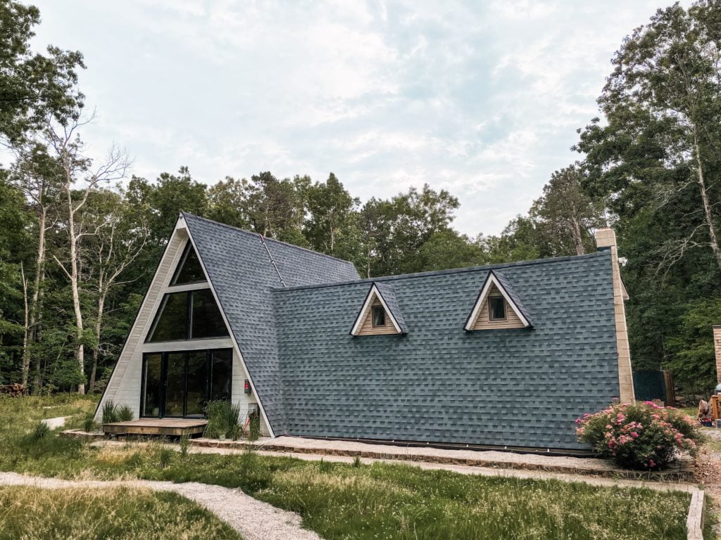 Lokal Aframe Triangle House with white cladding, large wall of windows and black shingle roof with path winding in landscape in front of it.
