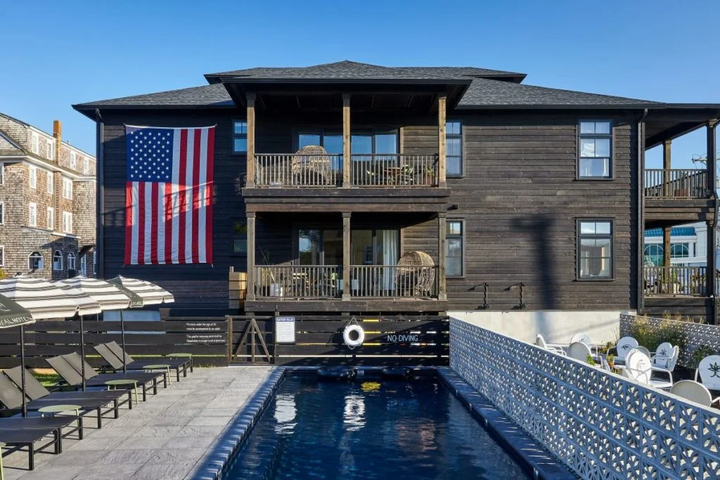 A large dark brown building with a pool and lounge chairs in front of it.